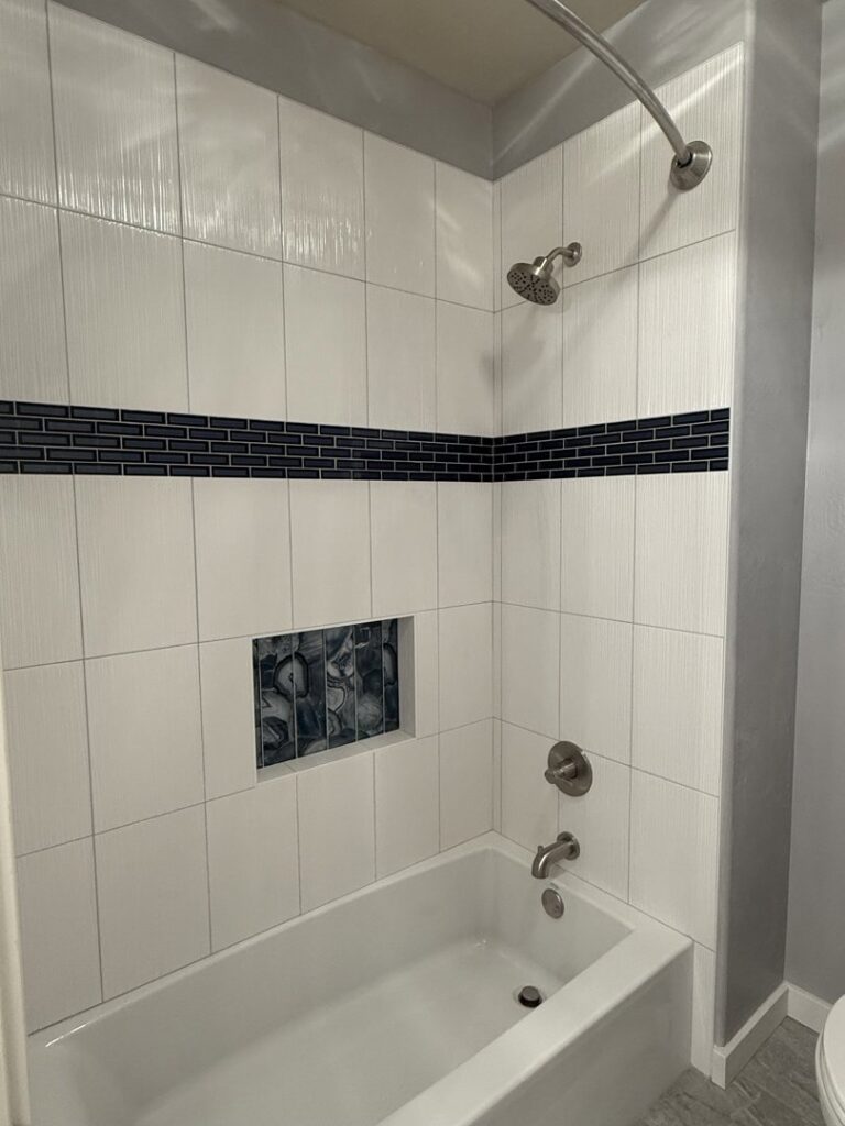A newly installed bathtub with white subway tiles and a dark accent stripe by AZ New Bath in Glendale, AZ