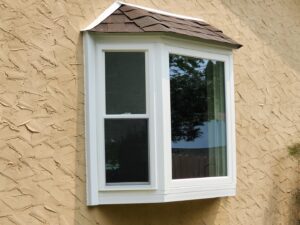 A newly installed bay window with a small shingled roof on a textured wall by The Window Man of Ohio in Westerville, OH.