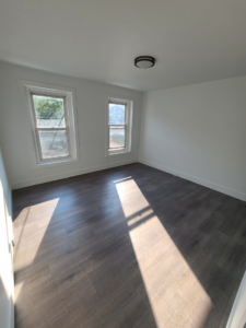 A bright bedroom with dark wood-look flooring and two windows, completed by Modern Image Construction LLC in El Paso, TX