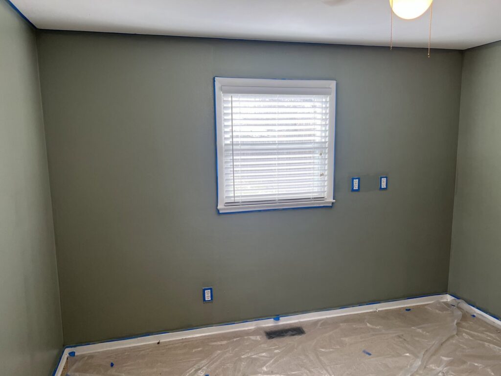 A bedroom prepared for painting with green walls, blue painter's tape, and floor coverings by JW Contracting Services, LLC in Dayton, OH.