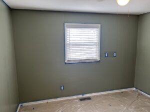 A bedroom prepared for painting with green walls, blue painter's tape, and floor coverings by JW Contracting Services, LLC in Dayton, OH.