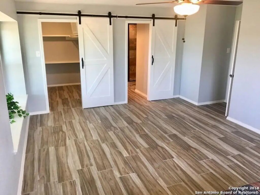 A renovated bedroom featuring wood-look tile flooring and stylish white barn doors by Morin Construction LLC in San Antonio, TX