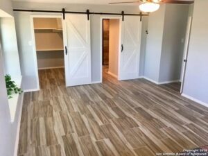 A renovated bedroom featuring wood-look tile flooring and stylish white barn doors by Morin Construction LLC in San Antonio, TX