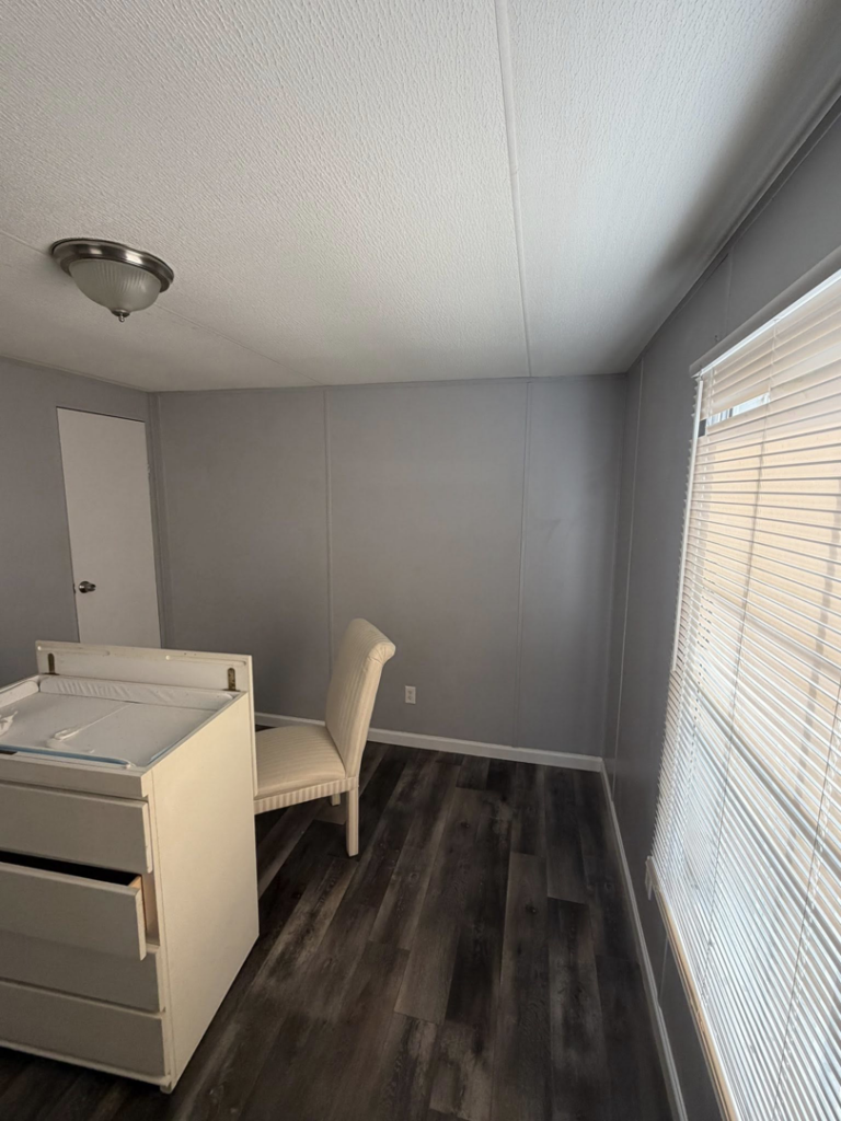 A renovated bedroom featuring new dark laminate flooring, freshly painted gray walls, and a light fixture by Hard Knox Handyman in Knoxville, TN.