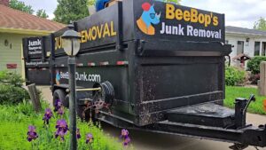 A BeeBop's Junk Removal branded trailer loaded with various junk items in a residential driveway in Sioux Falls, SD.