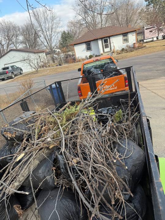 A BeeBop's Junk Removal trailer loaded with trash bags and tree branches, with the branded truck in Sioux Falls, SD.