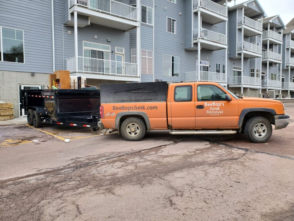 A BeeBop's Junk Removal truck and trailer at an apartment complex for a junk removal job in Sioux Falls, SD.