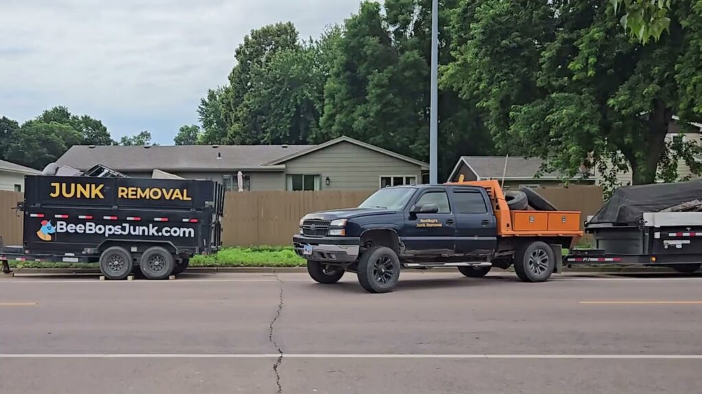 A BeeBop's Junk Removal truck towing two trailers, one branded for junk removal, parked on a street in Sioux Falls, SD.