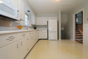 An older kitchen with white cabinets and yellow linoleum flooring, ready for a remodel by KLS Remodel in Cincinnati, OH.