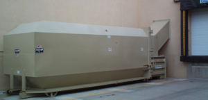A beige industrial waste compactor unit next to a loading dock at Jackson Compaction in Albuquerque, NM.