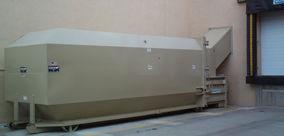 A beige industrial waste compactor unit next to a loading dock at Jackson Compaction in Albuquerque, NM.
