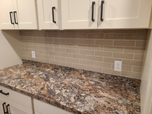 A newly installed beige subway tile backsplash and white cabinets with black handles by Bryan's Home Services in Fargo, ND.