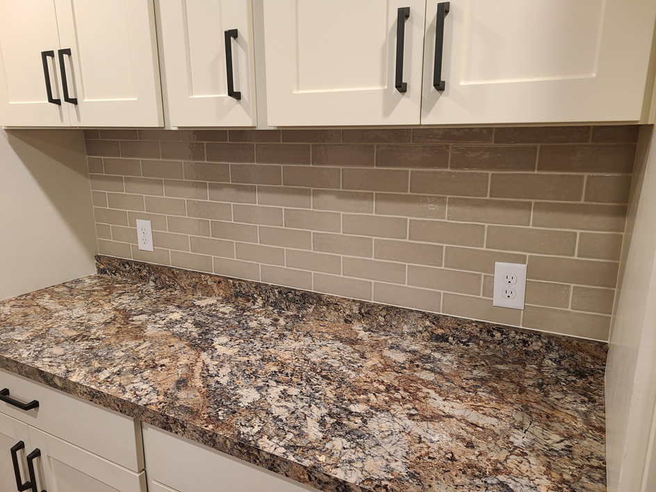 A newly installed beige subway tile backsplash and white cabinets with black handles by Bryan's Home Services in Fargo, ND.