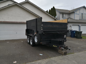 A black BigTex dump trailer with wooden side extensions parked in a residential driveway, used for junk removal by Gorilla Hauling in Kent, WA.