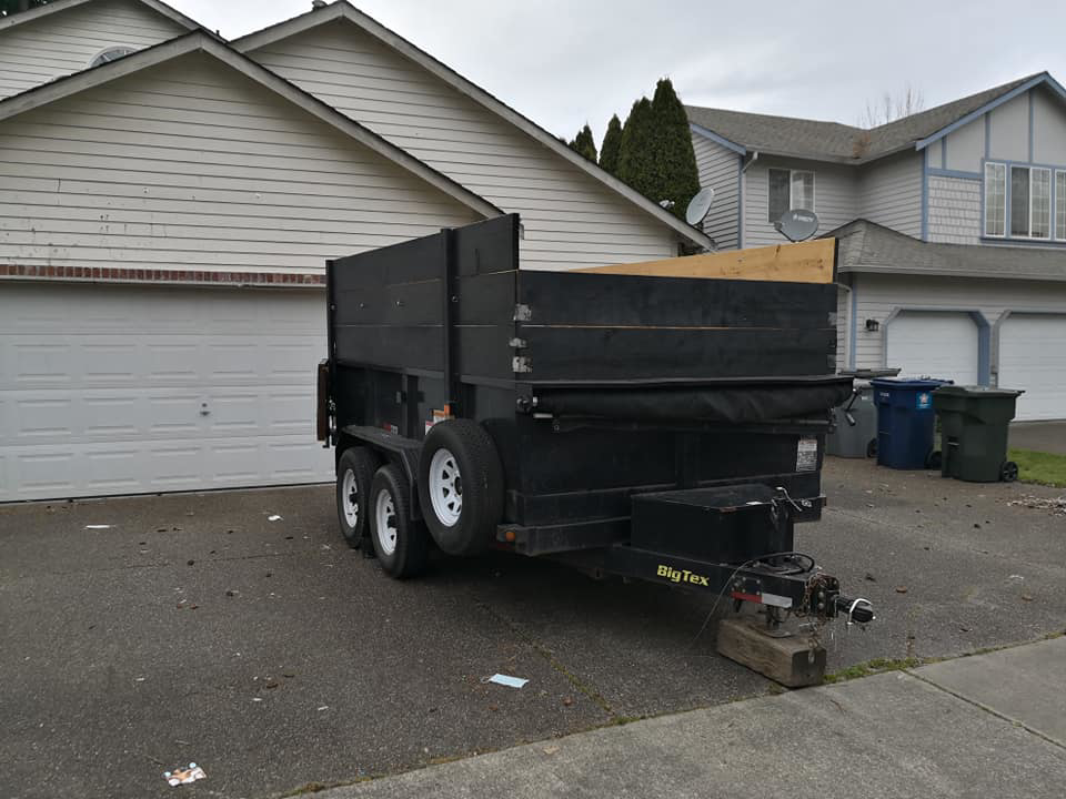 A black BigTex dump trailer with wooden side extensions parked in a residential driveway, used for junk removal by Gorilla Hauling in Kent, WA.