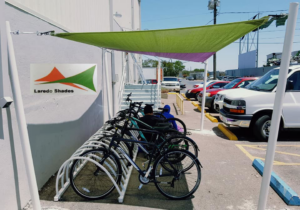 A green and purple shade sail installed over a bike rack by Laredo Shades, a general contractor in Laredo, TX.