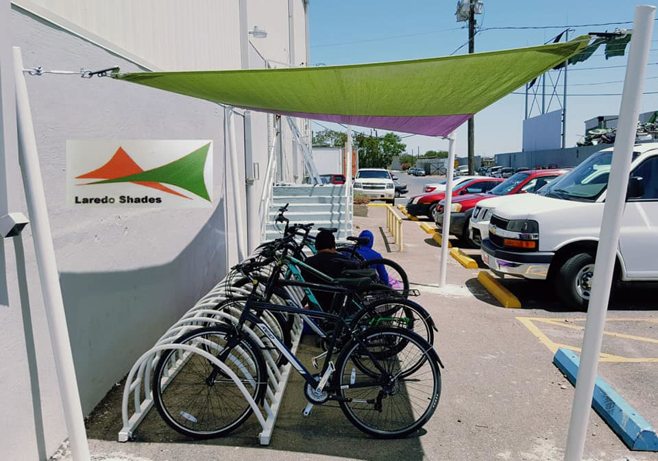 A green and purple shade sail installed over a bike rack by Laredo Shades, a general contractor in Laredo, TX.