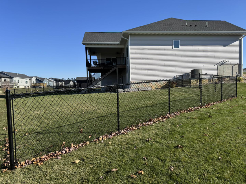 A newly installed black chain-link fence enclosing a residential backyard by Bergmann Fencing Co. in Cedar Falls, IA.