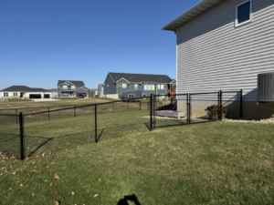 A black chain-link fence with a gate providing access to a residential backyard, installed by Bergmann Fencing Co. in Cedar Falls, IA.