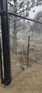 Installation of a black chain-link fence post with a yellow cable by Michel's Fencing in Bend, OR