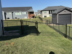 A black chain-link fence installed along a sloped residential backyard by Bergmann Fencing Co. in Cedar Falls, IA.