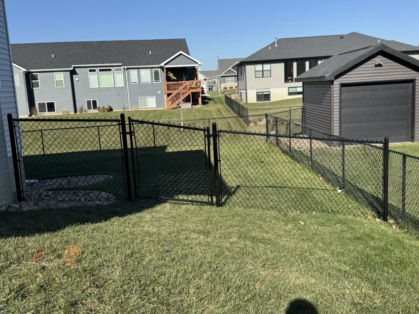 A black chain-link fence installed along a sloped residential backyard by Bergmann Fencing Co. in Cedar Falls, IA.