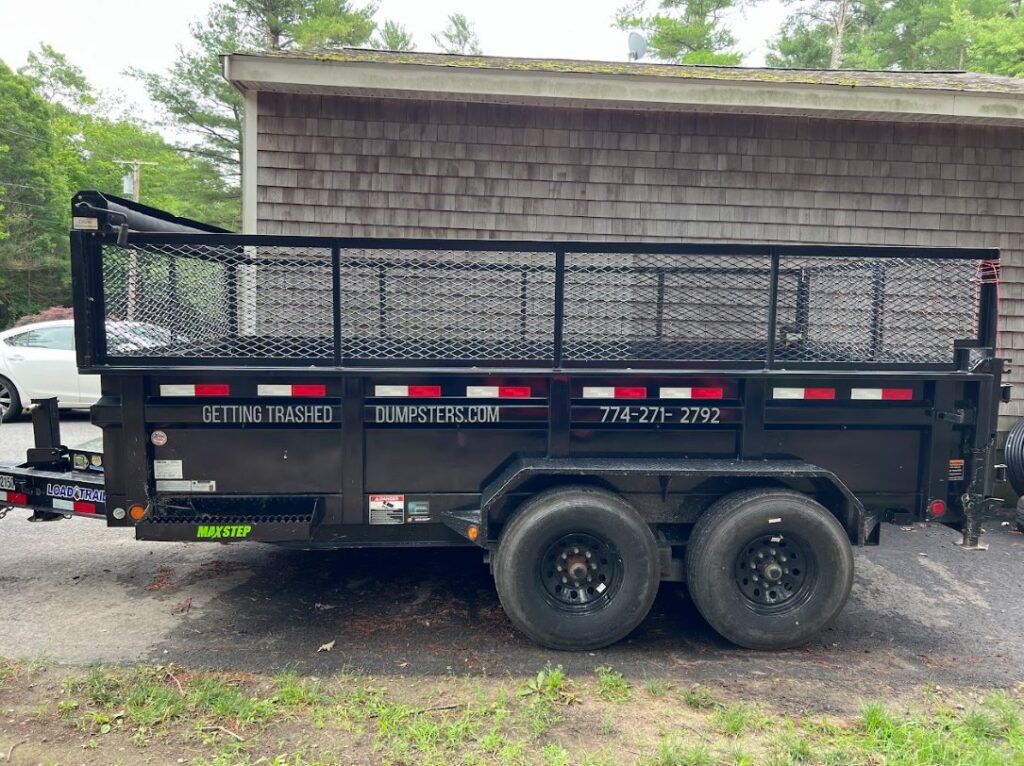 A black dump trailer with the business name on its side, parked for Getting Trashed Dumpster Rentals & Excavation in Assonet, MA.