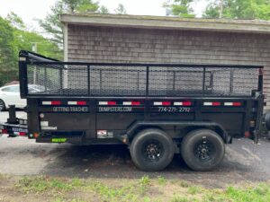A black dump trailer with the business name on its side, parked for Getting Trashed Dumpster Rentals & Excavation in Assonet, MA.