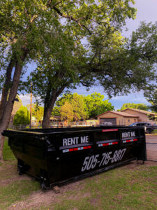 A black dump trailer from Duke City Dumpster Rentals LLC parked in a residential grassy yard, available for junk removal in Albuquerque, NM.