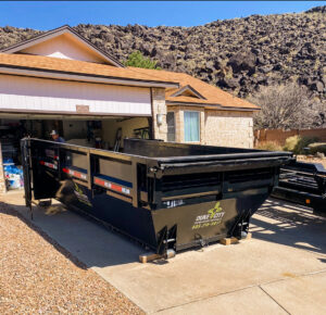 A black dump trailer from Duke City Dumpster Rentals LLC parked in a residential driveway in Albuquerque, NM, ready for a junk removal project.