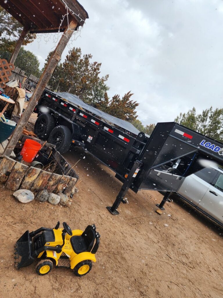 A black dump trailer from Bin Suave LLC parked in a residential yard, ready for junk removal in Espanola, NM.
