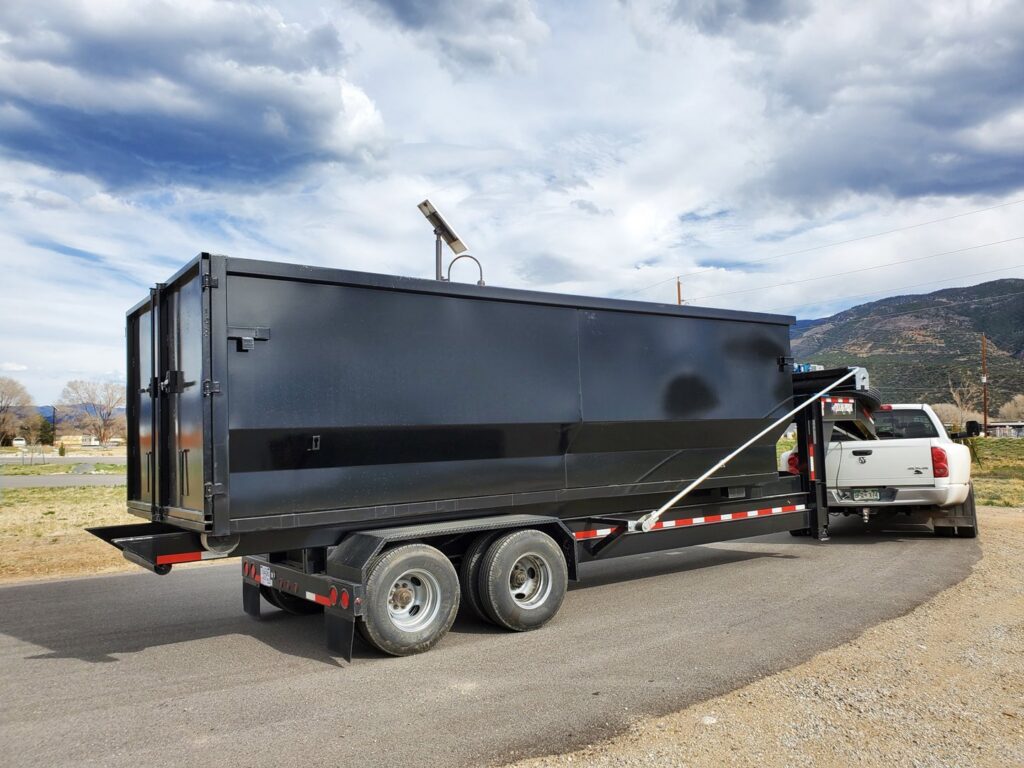 A black dump trailer towed by a white pickup truck, ready for junk removal by Arkansas Valley Roll-Off in Salida, CO.