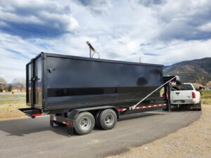 A black dump trailer towed by a white pickup truck, ready for junk removal by Arkansas Valley Roll-Off in Salida, CO.