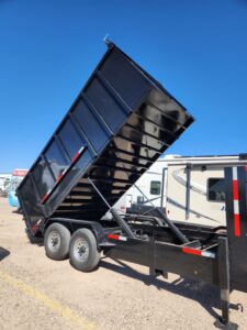 A black dump trailer with its bed raised, in the process of unloading junk for Jigsaw Transport and Waste in Albuquerque, NM.