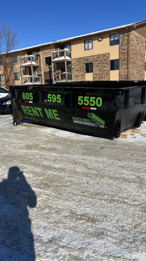 A black dumpster from Waste-Away Dumpsters & Disposal LLC placed outside an apartment complex in Sioux Falls, SD.