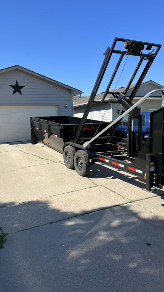 A black dumpster being loaded onto a trailer by Waste-Away Dumpsters & Disposal LLC for junk removal in Sioux Falls, SD.