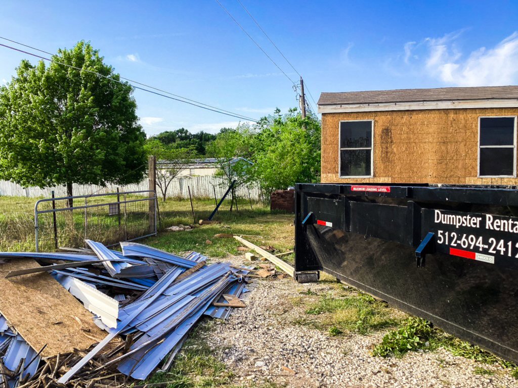 A black dumpster from Liberty Hill Dumpster Rental next to a pile of construction debris at a job site in Austin, TX