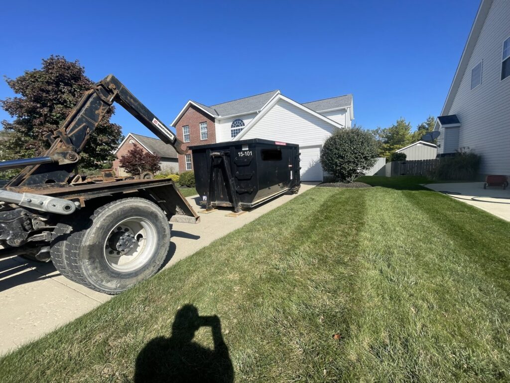 A black dumpster being delivered or picked up on a residential driveway by Lil Man W/A Can LLC in Columbus, OH.