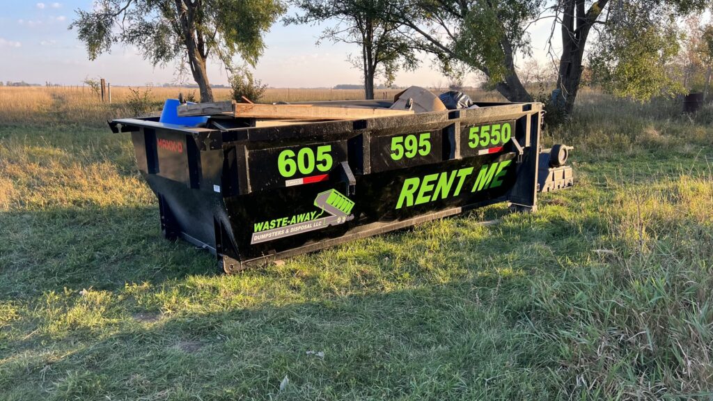 A black dumpster from Waste-Away Dumpsters & Disposal LLC filled with junk in a rural area near Sioux Falls, SD.