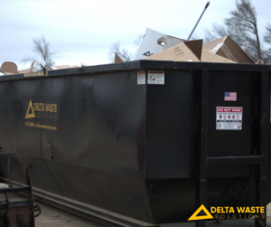 A black Delta Waste Solutions dumpster filled with cardboard boxes and debris, demonstrating junk removal services in Hattiesburg, MS.