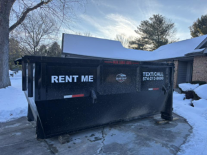 A black dumpster from Dump that Junk LLC placed in a snowy residential driveway in Mishawaka, IN.
