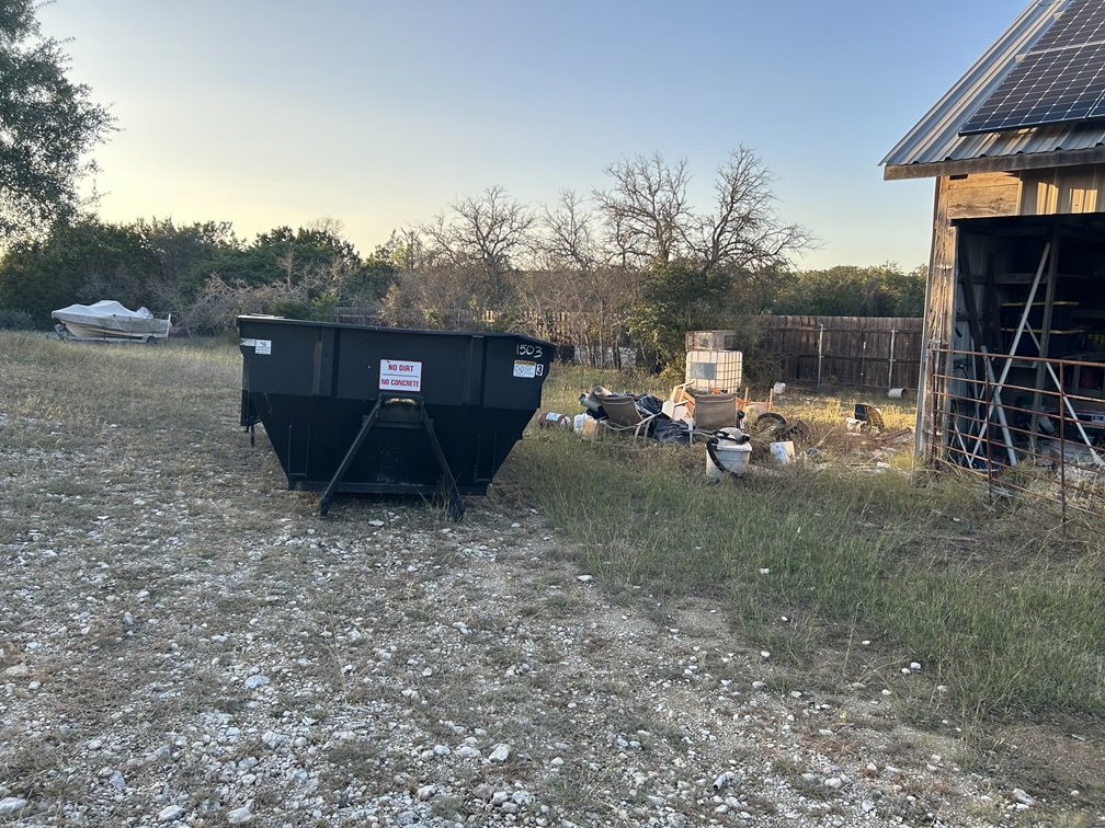A black dumpster from Liberty Hill Dumpster Rental next to a pile of junk outside a building in Austin, TX