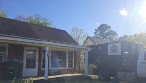 A black dumpster being loaded onto a truck in front of a residential house by Beetles Dumpsters Rental & Junk Removal in Huntsville, AL.