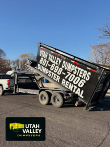 A black dumpster on a trailer being transported by Utah Valley Dumpsters in Provo, UT.