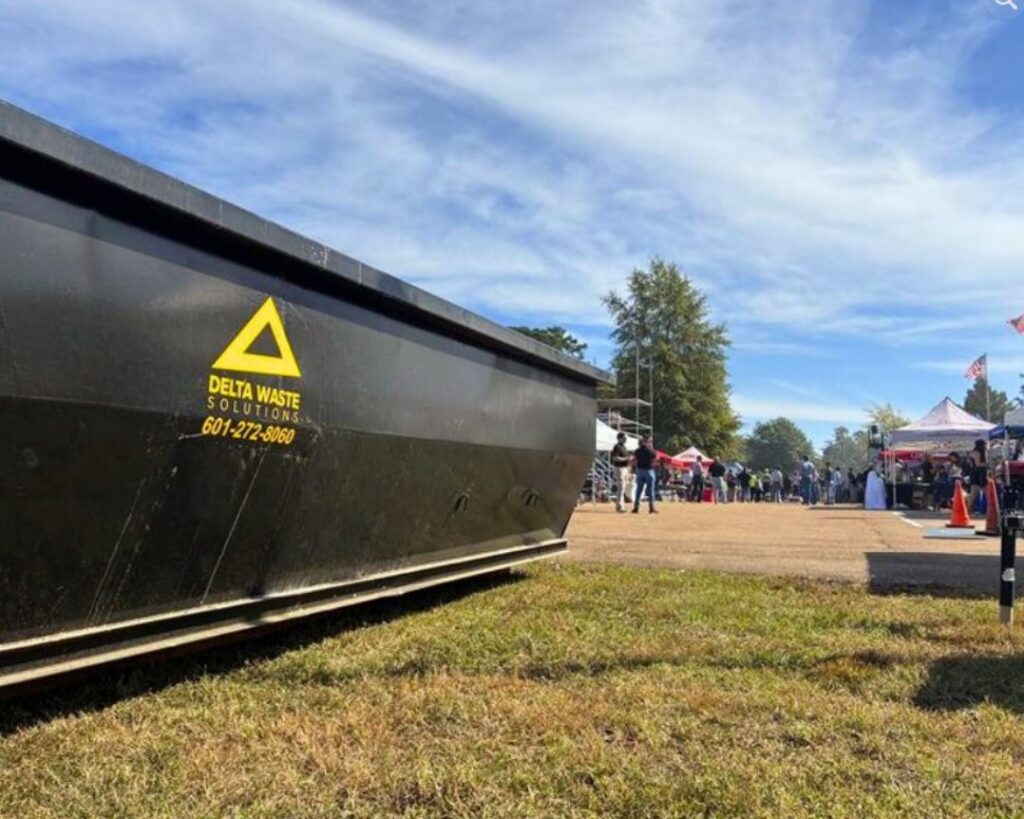 A black Delta Waste Solutions dumpster at an outdoor event, providing junk removal and waste management services in Hattiesburg, MS.