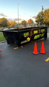 A black dumpster from Waste-Away Dumpsters & Disposal LLC in a parking lot with traffic cones in Sioux Falls, SD.