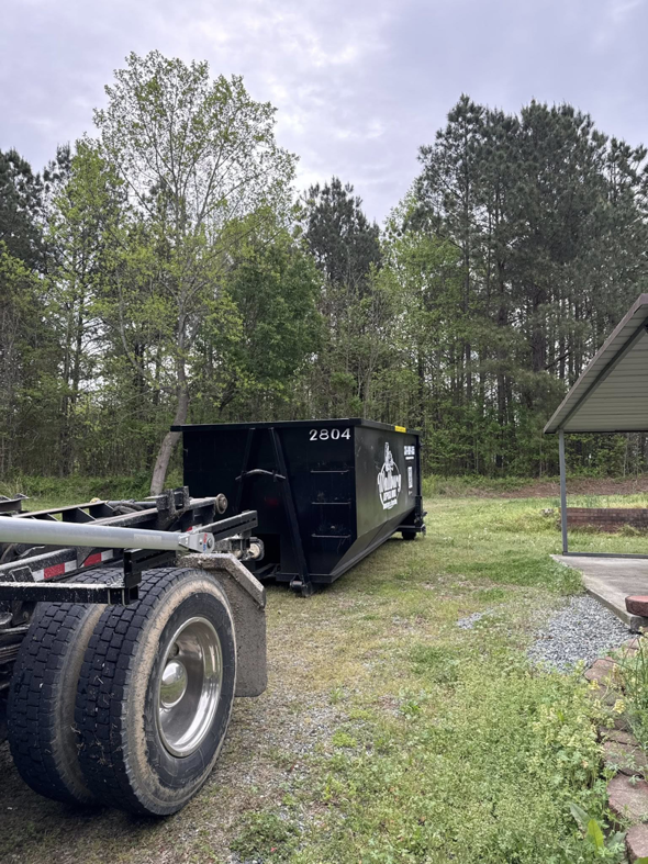 A black Wallburg Disposal Worx LLC dumpster placed in a grassy area for junk removal in High Point, NC.