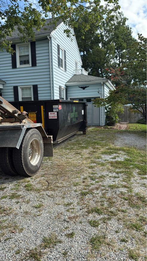 A black dumpster being delivered to a residential home by Wood Property Services & Dumpster Rental LLC in Wilmington, NC.
