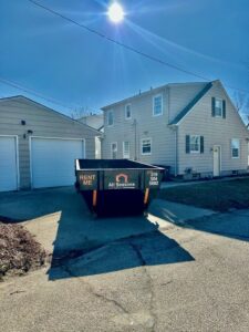 A black dumpster with the business logo placed on a residential driveway by All Seasons Junk Removal & Dumpster Services in Center Point, IA.