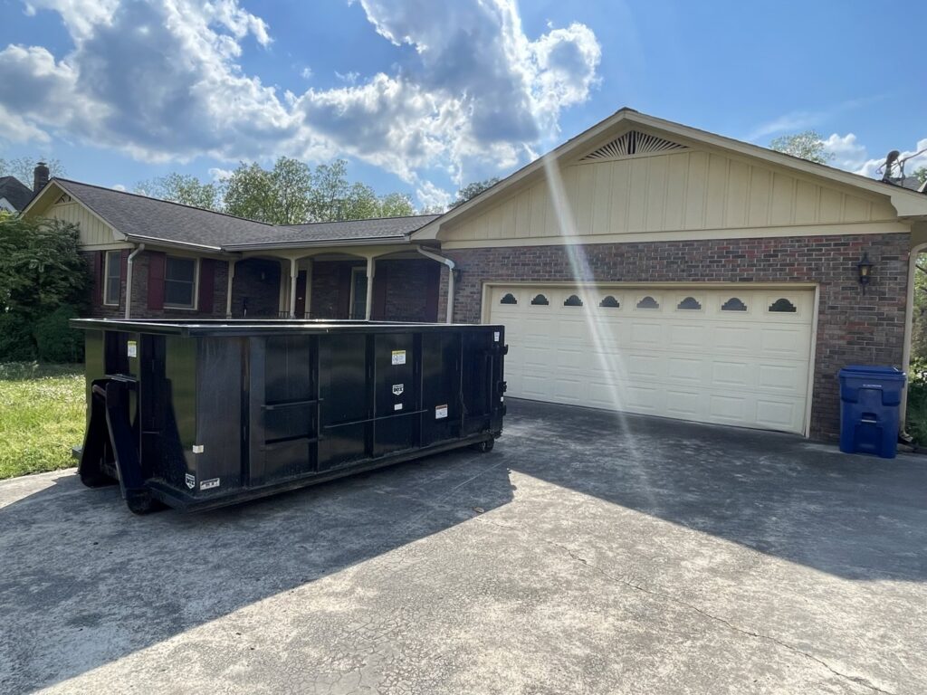 A black dumpster placed in a residential driveway by Beetles Dumpsters Rental & Junk Removal in Huntsville, AL.